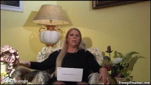 A Woman Is Sitting In A Chair With A Laptop In Front Of Her And A Lamp Behind Her GIF