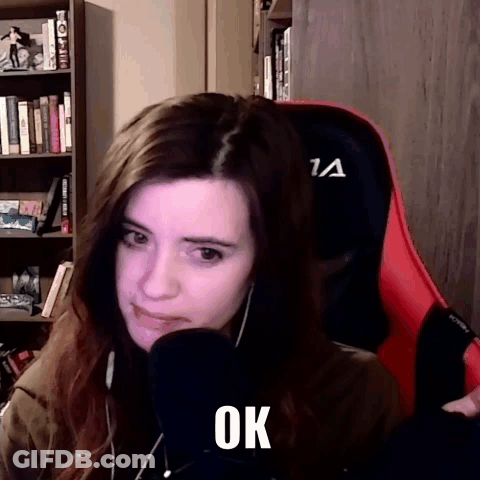 A Woman Is Sitting In A Chair With A Microphone In Front Of Her And The Word Ok Is On Her Face . GIF