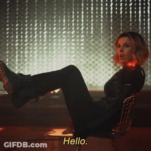 A Woman Is Sitting In A Chair With Her Feet Up And The Words Hello Behind Her GIF