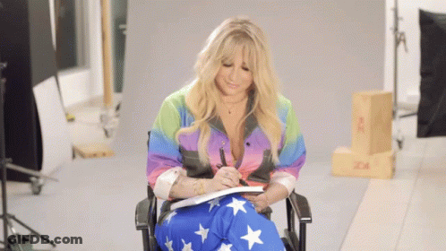 A Woman Is Sitting In A Chair Writing In A Notebook GIF