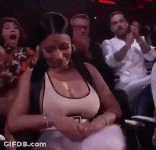A Woman Is Sitting In A Crowd Of People And Holding A Cell Phone . GIF