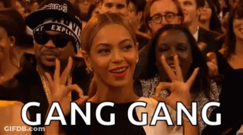 A Woman Is Sitting In A Crowd Of People Making A Peace Sign And The Word Gang Gang Is Written Above Her . GIF