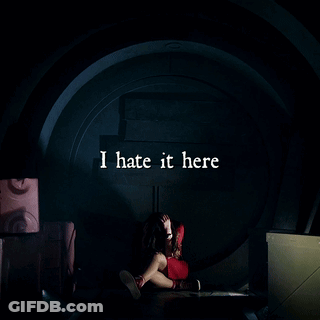 A Woman Is Sitting In A Dark Room With The Words I Hate It Here Written Above Her GIF