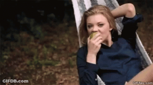 A Woman Is Sitting In A Hammock And Eating An Apple . GIF