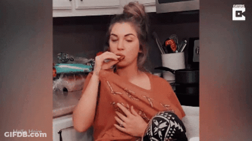 A Woman Is Sitting In A Kitchen Eating A Piece Of Food And The Words Hollie Haine Are On The Bottom GIF