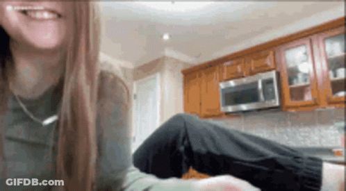 A Woman Is Sitting In A Kitchen With Her Legs Crossed And Smiling . GIF