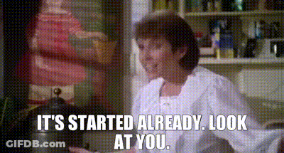 A Woman Is Sitting In A Kitchen With The Words `` It 'S Started Already Look At You '' Written On The Screen . GIF