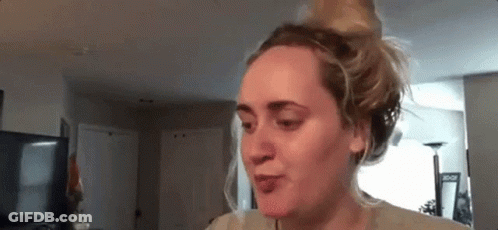 A Woman Is Sitting In A Living Room With Her Hair In A Bun And Making A Funny Face . GIF
