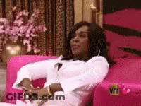 A Woman Is Sitting In A Pink Chair In A Living Room . GIF