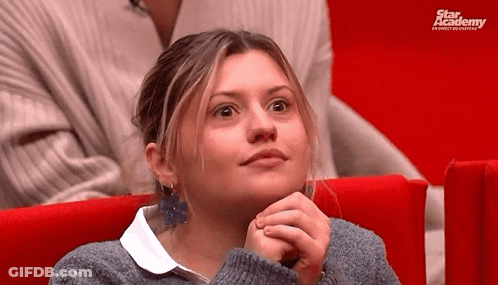 A Woman Is Sitting In A Red Chair With Her Hands On Her Chin . GIF