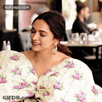 A Woman Is Sitting In A Restaurant Wearing A Floral Dress And Smiling . GIF