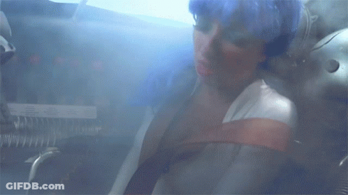 A Woman Is Sitting In A Room With A Smoke Coming Out Of Her Mouth GIF