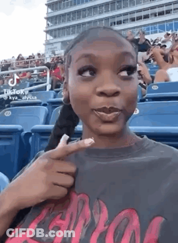 A Woman Is Sitting In A Stadium Holding A Piece Of Paper In Her Hand . GIF