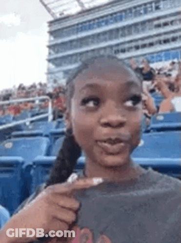 A Woman Is Sitting In A Stadium With A Ponytail And Pointing At Something . GIF