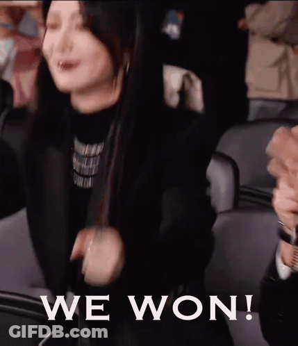 A Woman Is Sitting In A Stadium With Her Arms In The Air And The Words We Won Written On The Bottom . GIF