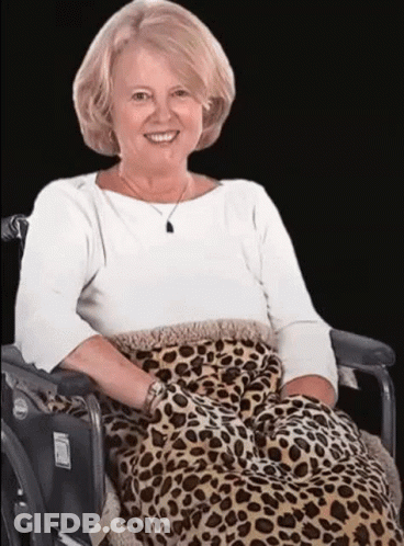 A Woman Is Sitting In A Wheelchair With A Leopard Print Blanket On Her Lap . GIF