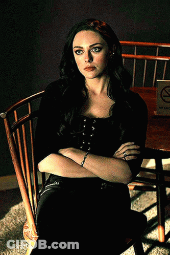 A Woman Is Sitting In A Wooden Chair With Her Arms Crossed In Front Of A No Smoking Sign GIF