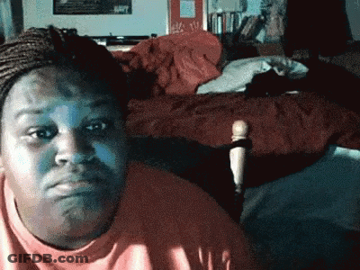 A Woman Is Sitting In Front Of A Bed And Making A Face GIF