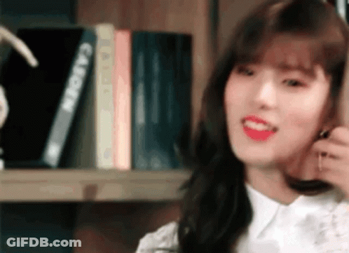 A Woman Is Sitting In Front Of A Bookshelf With Books . GIF