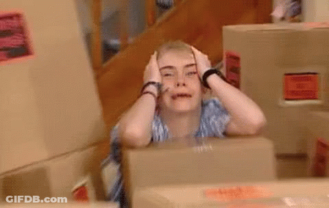 A Woman Is Sitting In Front Of A Box With Her Hands On Her Head And Making A Funny Face . GIF