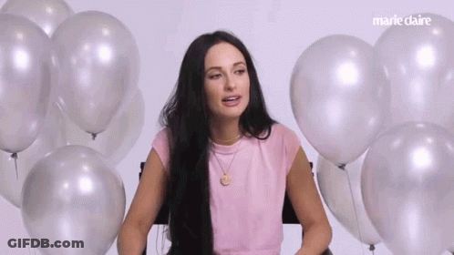 A Woman Is Sitting In Front Of A Bunch Of Balloons And Talking . GIF
