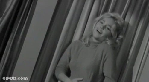 A Woman Is Sitting In Front Of A Curtain In A Black And White Photo GIF