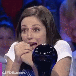 A Woman Is Sitting In Front Of A Glass Ball With Her Mouth Open And Looking At It . GIF