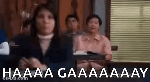 A Woman Is Sitting In Front Of A Group Of People In A Room And Making A Funny Face . GIF