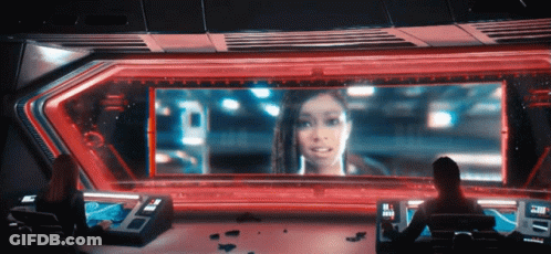 A Woman Is Sitting In Front Of A Large Screen That Says ' A ' On It GIF