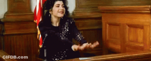 A Woman Is Sitting In Front Of A Microphone In A Courtroom With Her Hands Outstretched . GIF