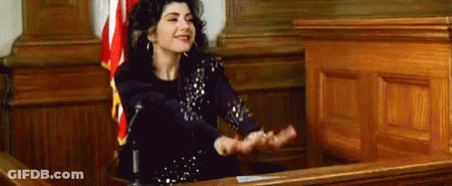 A Woman Is Sitting In Front Of A Microphone In A Courtroom With Her Hands Outstretched . GIF