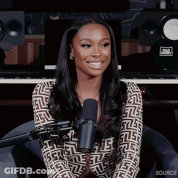 A Woman Is Sitting In Front Of A Microphone In A Recording Studio And Smiling . GIF