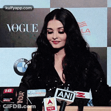 A Woman Is Sitting In Front Of A Microphone In Front Of A Sign That Says Vogue . GIF