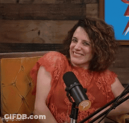 A Woman Is Sitting In Front Of A Microphone With Her Eyes Closed And Her Hands In The Air GIF