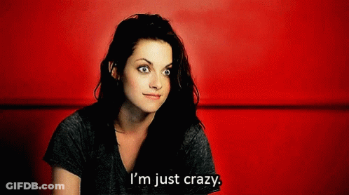 A Woman Is Sitting In Front Of A Red Wall And Says " I 'M Just Crazy " GIF