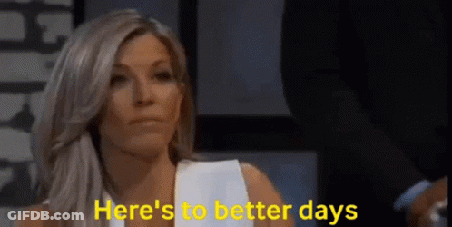 A Woman Is Sitting In Front Of A Sign That Says Here 'S To Better Days GIF