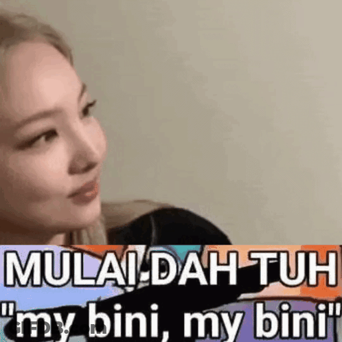 A Woman Is Sitting In Front Of A Wall With A Sticker That Says Mulai Dah Tuh My Bini My Bini . GIF