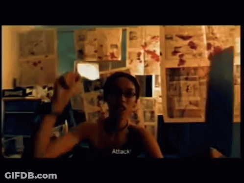 A Woman Is Sitting In Front Of A Wall With Pictures And The Word Attack Is On The Screen GIF