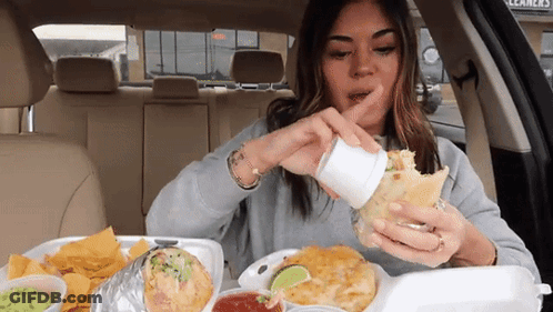 A Woman Is Sitting In The Back Seat Of A Car Eating A Burrito And Chips . GIF