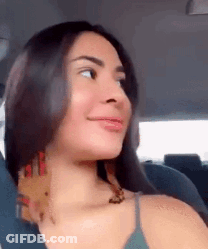 A Woman Is Sitting In The Back Seat Of A Car Looking At The Camera . GIF