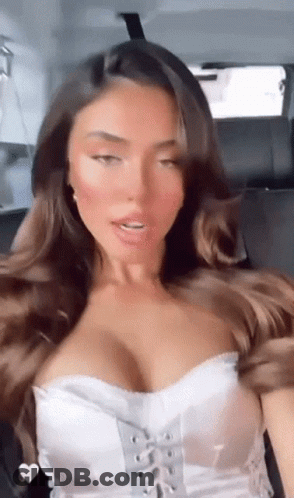 A Woman Is Sitting In The Back Seat Of A Car Wearing A White Top . GIF