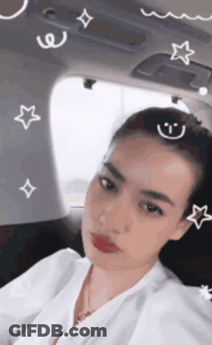 A Woman Is Sitting In The Back Seat Of A Car With A Smiley Face And Stars On Her Head . GIF