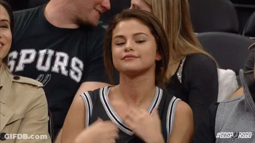A Woman Is Sitting In The Stands At A Basketball Game Wearing A Spurs Shirt . GIF