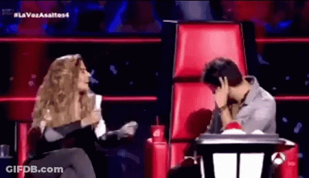 A Woman Is Sitting Next To A Man In A Red Chair Covering His Face With His Hand . GIF