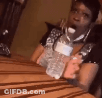 A Woman Is Sitting On A Bed Holding A Bottle Of Water And A Cell Phone . GIF