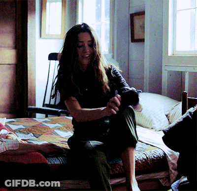 A Woman Is Sitting On A Bed With A Quilt On It GIF