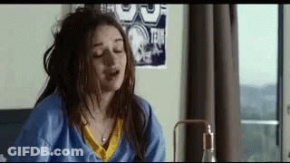 A Woman Is Sitting On A Bed With Her Eyes Closed And Her Hair In A Bun . GIF