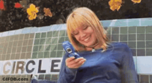 A Woman Is Sitting On A Bench Holding A Cell Phone In Front Of A Sign That Says Circle . GIF