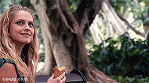 A Woman Is Sitting On A Bench Holding An Ice Cream Cone And Smiling . GIF