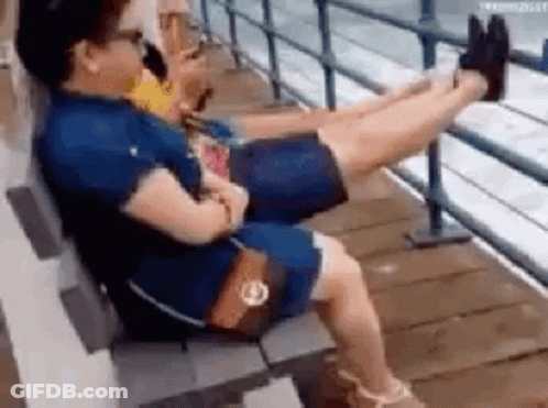A Woman Is Sitting On A Bench With Her Feet Up On A Railing . GIF